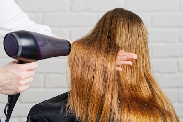 Hermosa mujer joven en la peluquería que se seca el cabello con secador de pelo en el salón