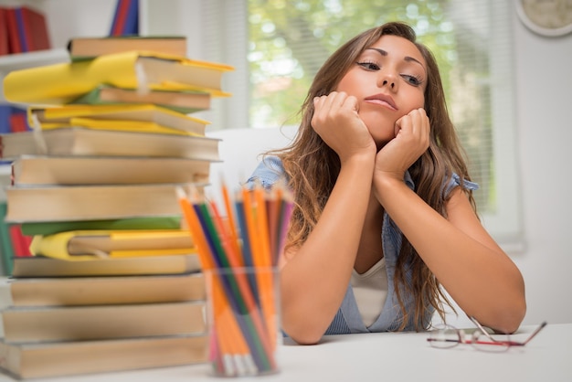 Hermosa mujer joven pensativa con el pensamiento de muchos libros en la biblioteca.