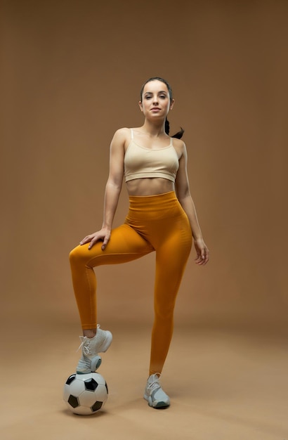 Hermosa mujer joven con pie de balón de fútbol en el estudio