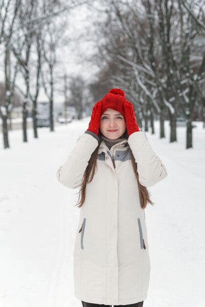 Hermosa mujer joven de pie y endereza su sombrero entre los árboles nevados en el bosque de invierno. Marco vertical.