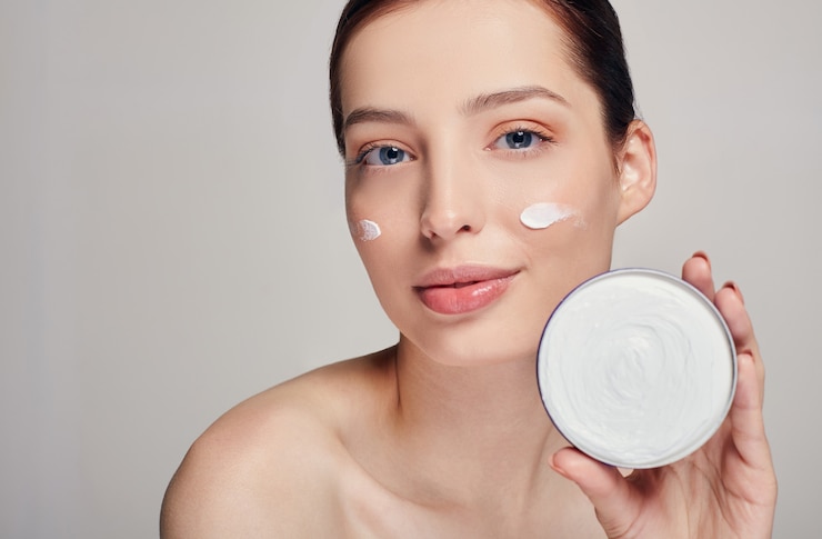 Foto hermosa mujer joven con piel limpia y fresca con ojos azules y cabello oscuro tiene crema cerca de su cara. tratamiento de belleza facial. cosmetología.