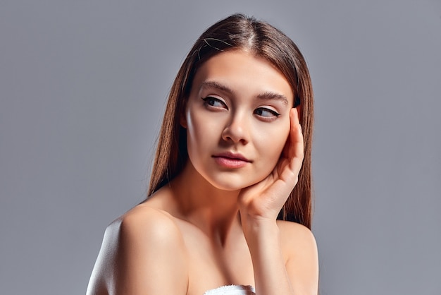 Hermosa mujer joven con piel limpia perfecta. Retrato de modelo de belleza con maquillaje nude natural. Spa, cuidado de la piel y bienestar. De cerca, fondo gris, copyspace.