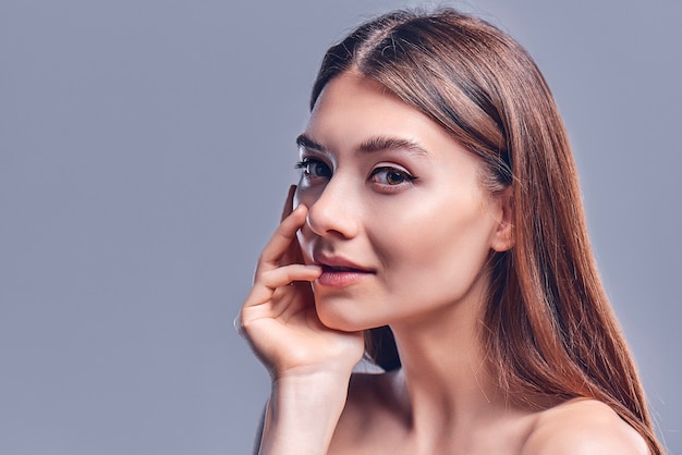 Hermosa mujer joven con piel limpia perfecta. Retrato de modelo de belleza con maquillaje nude natural. Spa, cuidado de la piel y bienestar. De cerca, fondo gris, copyspace.