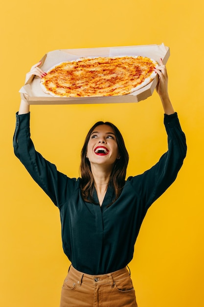 Hermosa mujer joven con pizza posando sobre un fondo amarillo