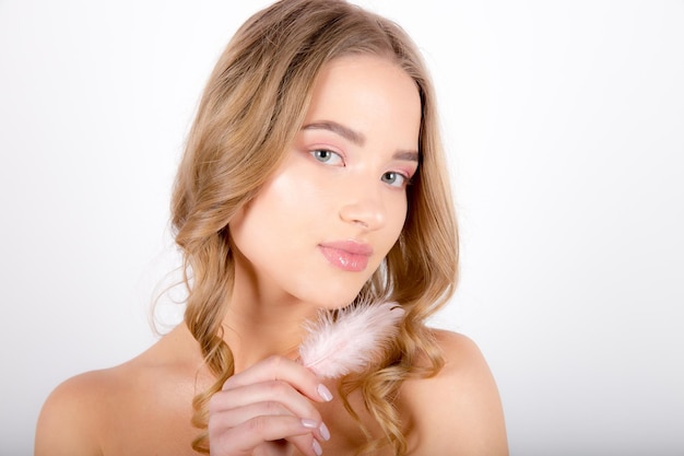 Hermosa mujer joven posando aislada sobre fondo de pared blanca con pluma