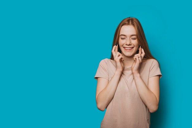 Hermosa mujer joven posando contra una pared azul con los dedos cruzados sonriendo.