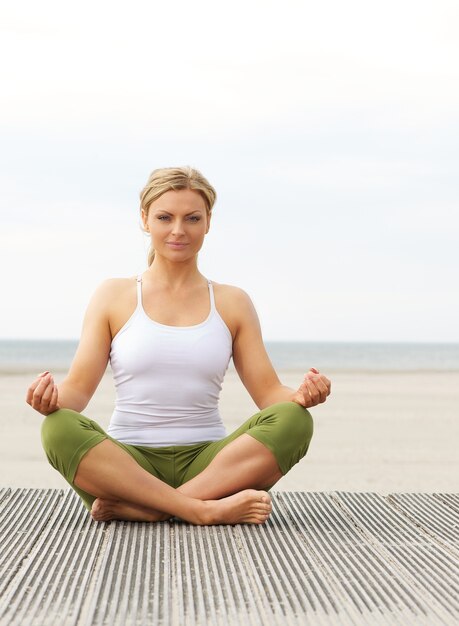 Hermosa mujer joven en pose de yoga en la playa