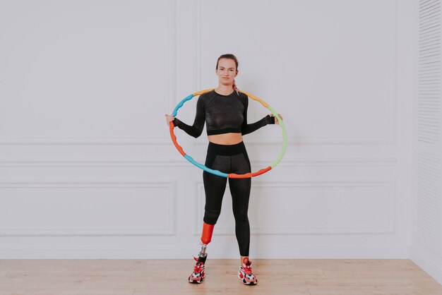 Foto hermosa mujer joven con prótesis de pierna, con hula hoop