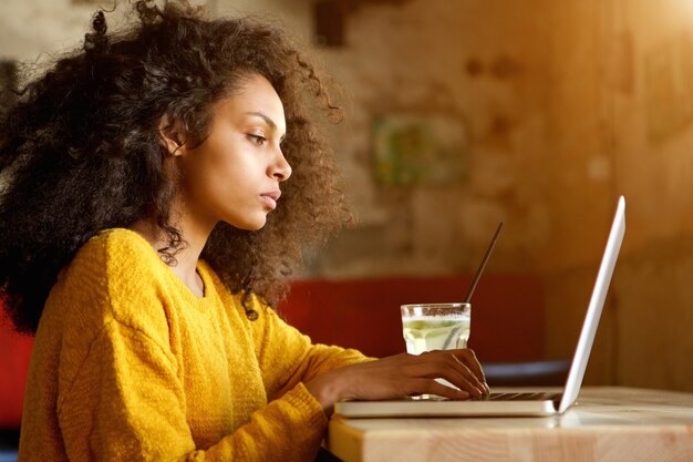 Hermosa mujer joven que trabaja en la computadora portátil en un café