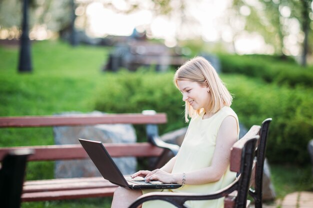 Hermosa mujer joven que trabaja en la computadora portátil en el parque chica freelancer en la naturaleza