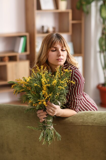 Hermosa mujer joven con ramo de flores de mimosa en casa