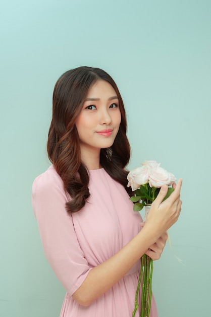 Hermosa mujer joven con un ramo de flores rosas sobre un fondo claro