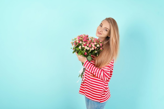 Hermosa mujer joven con ramo de rosas sobre fondo de color