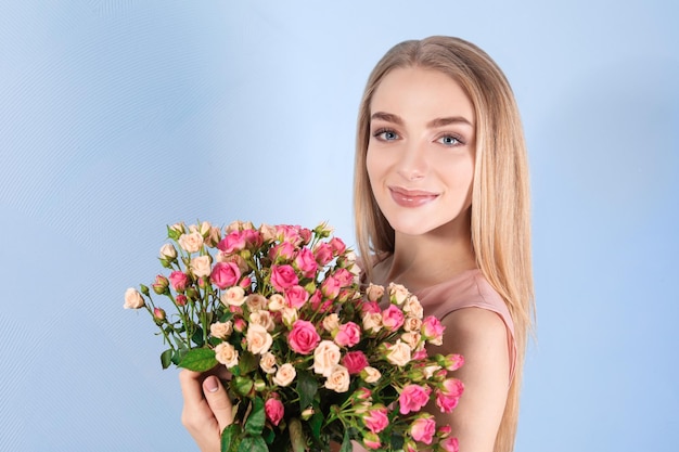 Hermosa mujer joven con ramo de rosas sobre fondo de color