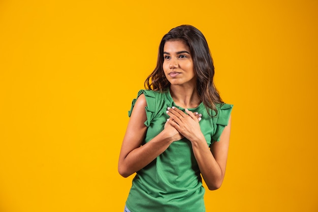 Hermosa mujer joven de raza mixta positiva amistosa con admirable sonrisa sincera sintiendo gratitud y agradecimiento, mostrando su corazón lleno de amor y gratitud tomados de la mano en el pecho