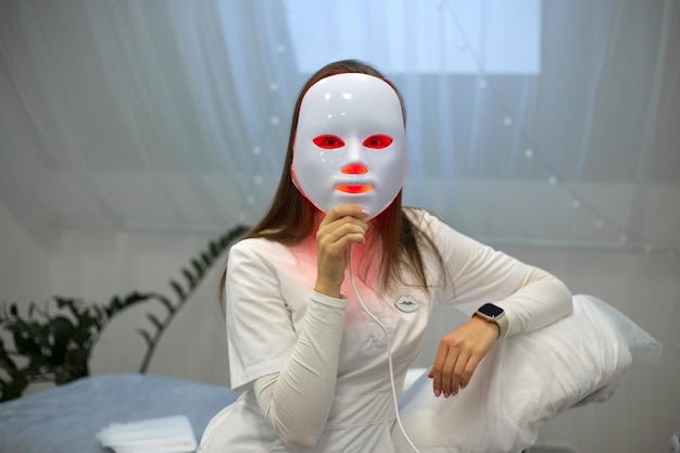 Hermosa mujer joven recibiendo un tratamiento de máscara de terapia de luz LED para su cara