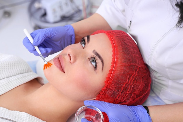 Foto hermosa mujer joven está recibiendo tratamiento para la piel de la cara. médico médico con un pincel para aplicar un fármaco terapéutico.