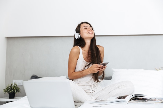 Hermosa mujer joven relajándose en la cama en casa, escuchando música con auriculares