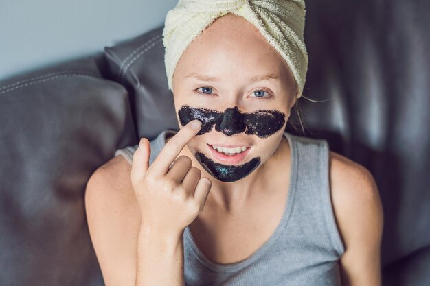 Hermosa mujer joven relajante con mascarilla en casa. Mujer alegre feliz aplicando máscara negra en la cara