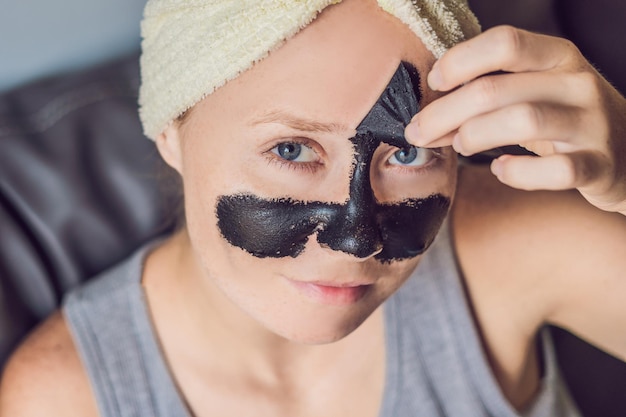 Hermosa mujer joven relajante con mascarilla en casa. Mujer alegre feliz aplicando máscara negra en la cara