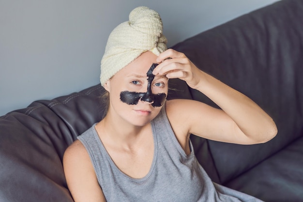 Hermosa mujer joven relajante con mascarilla en casa. Mujer alegre feliz aplicando máscara negra en la cara