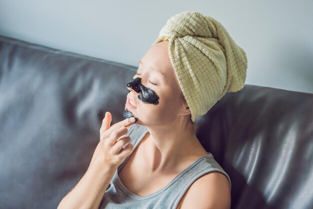 Hermosa mujer joven relajante con mascarilla en casa. Mujer alegre feliz aplicando máscara negra en la cara