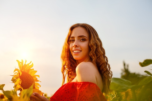 Hermosa mujer joven rizada en campo de girasol con flor de girasol en la mano retrato de joven w ...