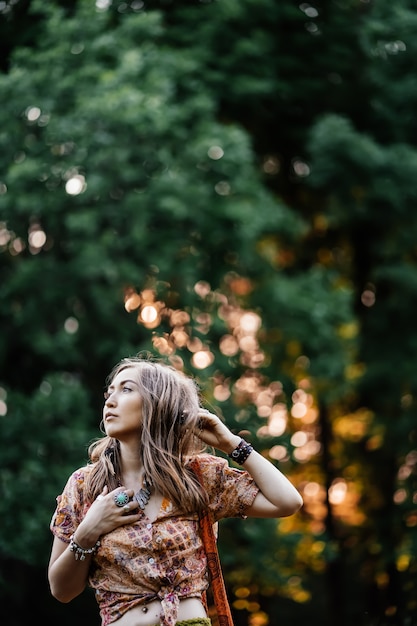 Foto hermosa mujer joven con ropa bohostyle posando en los rayos del sol de la tarde, puesta de sol. moda de estilo boho, mujer con joyas de plata divirtiéndose en el parque al aire libre.