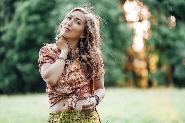 Hermosa mujer joven con ropa bohostyle posando en los rayos del sol de la tarde, puesta de sol. Moda de estilo boho, mujer con joyas de plata divirtiéndose en el parque al aire libre.