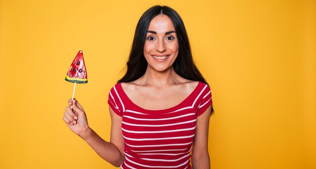 Hermosa mujer joven en ropa casual con piruleta en las manos posando sobre fondo naranja