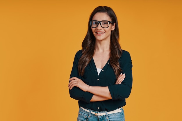 Hermosa mujer joven en ropa casual sonriendo y manteniendo los brazos cruzados