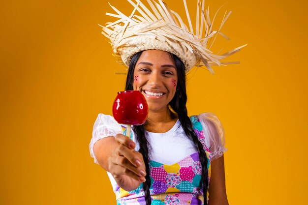 Hermosa mujer joven en ropa de fiesta de junio comiendo postre Love Apple Apple cubierto de caramelo rojo