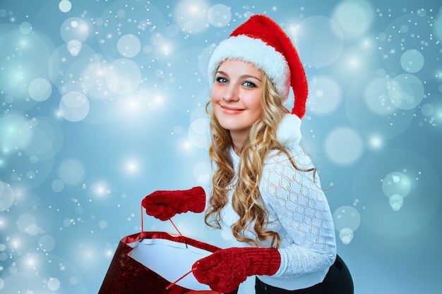 Hermosa mujer joven en ropa de Santa Claus con un regalo sobre un fondo azul.