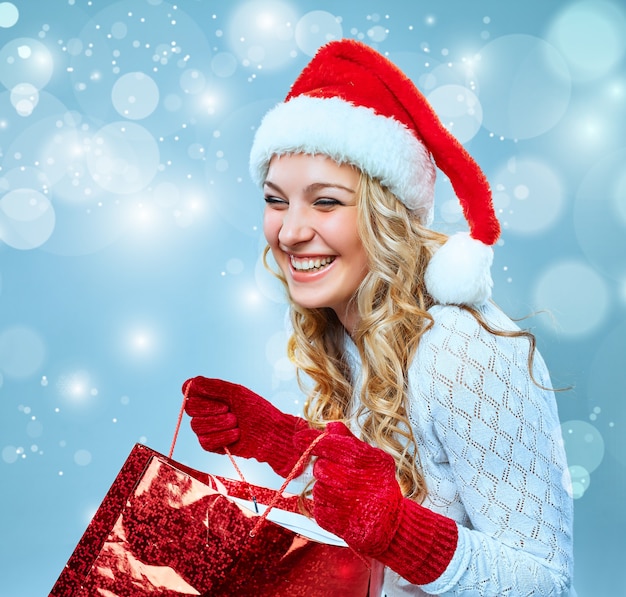 Hermosa mujer joven en ropa de Santa Claus con un regalo sobre un fondo azul.