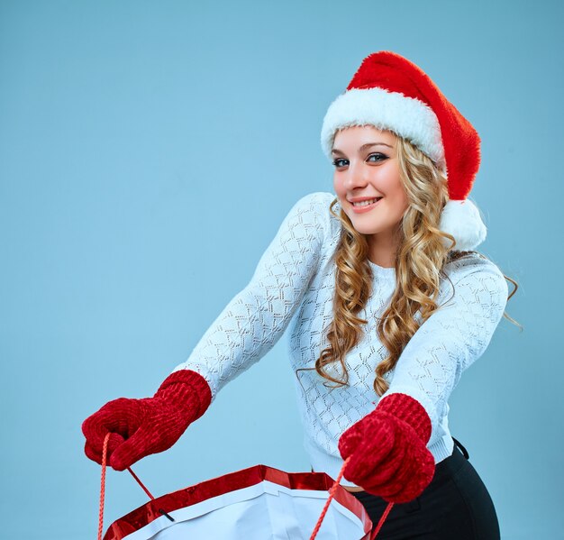 Hermosa mujer joven en ropa de Santa Claus con un regalo sobre un fondo azul.