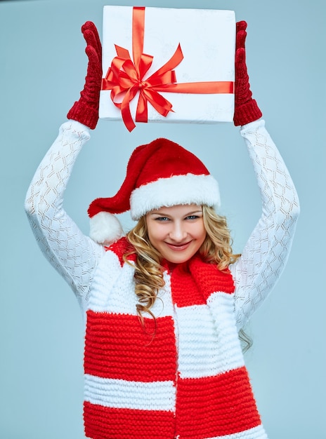 Hermosa mujer joven en ropa de Santa Claus con un regalo sobre un fondo gris