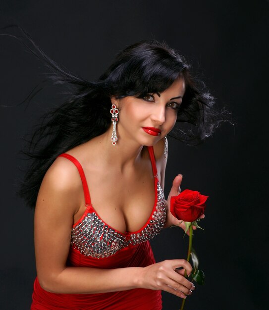 Foto hermosa mujer joven con rosa roja sobre fondo oscuro