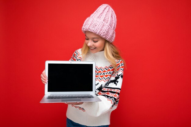 Hermosa mujer joven rubia sonriente encantadora sosteniendo la computadora portátil con vacío