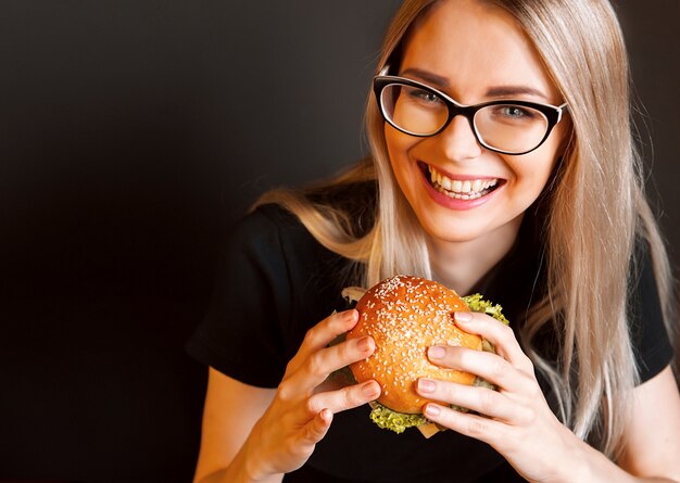 Hermosa mujer joven y saludable sostiene una sabrosa hamburguesa grande con chuleta de ternera