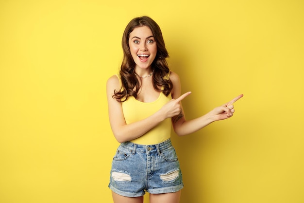 Hermosa mujer joven señalando con el dedo el logotipo de la pancarta o el anuncio sonriendo asombrada de pie en su...