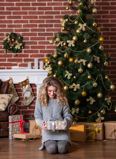 Hermosa mujer joven sentada cerca del árbol de Navidad decorado. Concepto de vacaciones de Navidad, año nuevo e invierno.