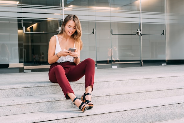 Hermosa mujer joven sentada en las escaleras en el teléfono móvil