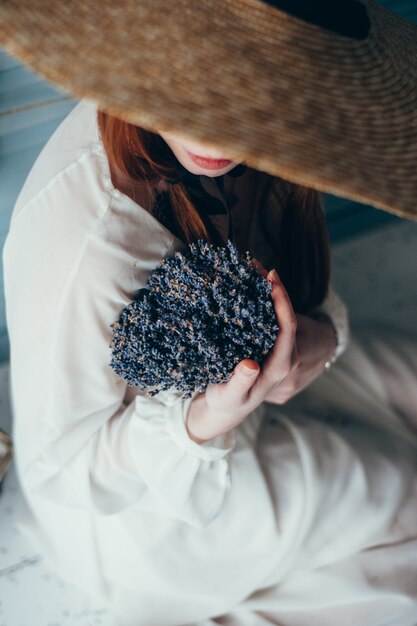 Hermosa mujer joven sentada con lavanda contra la pared azul.