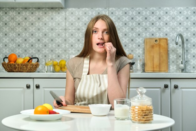 Hermosa mujer joven sentada a la mesa en la cocina con productos de frutas tabla de cortar cuchillo