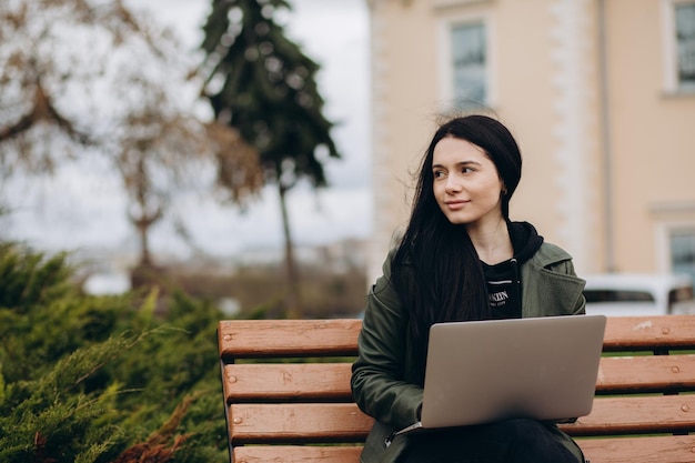 Hermosa mujer joven sentada en un parque público charlando sobre una computadora portátil