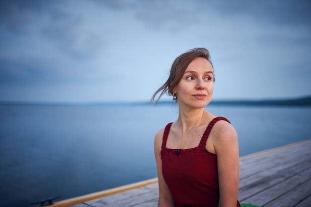 Hermosa mujer joven sentada en la terraza de madera cerca del lago