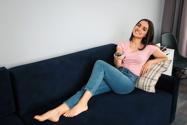 Hermosa mujer joven sentarse en el sofá y posar en la cámara. Ella sostiene el cepillo en la mano. Modelo en habitacion. Ella luce feliz.