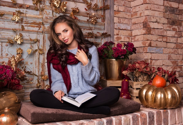 Hermosa mujer joven se sienta con un libro en el interior de otoño.