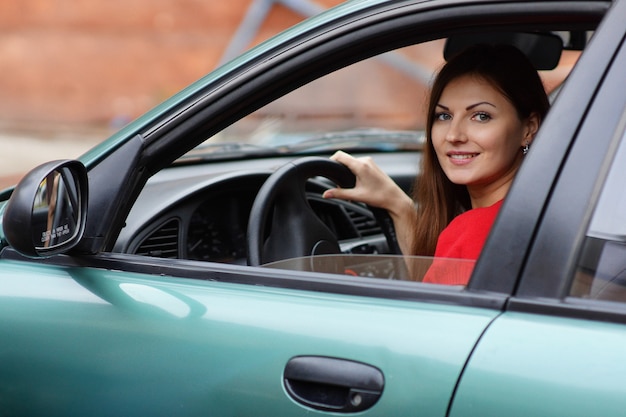 Hermosa mujer joven se sienta en un salón de autos al volante. entrenamiento de conducción. mujer conduciendo