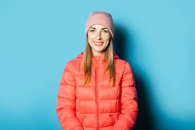 Hermosa mujer joven con un sombrero y una chaqueta de invierno sobre un fondo azul.